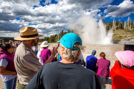 Ranger Terrance explains the mechanics of geysers, while a "grand" example erupts in the background