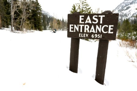 Snowmobiler rides westboud past the East Entrance sign photo