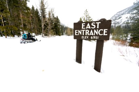 Snowmobiler rides eastboud past the East Entrance sign photo