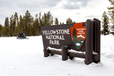 Snowmobilers drive past the West Entrance sign