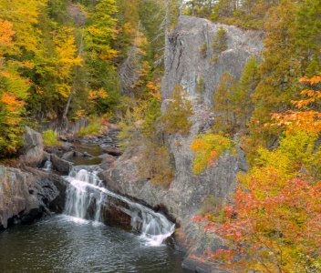 Rich fall foliage cheering up the cliffs of Buttermilk Falls on an overcast October day at Gulf Hagas in Maine. photo
