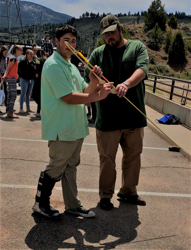 BLM Vernal FO Archaeologist Bill Reitze shows a student how to throw an atlatl at Flaming Gorge STEM Day. Flaming Gorge Dam, UT. Photo by BLM Utah