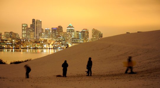 Sledders gaze at the city, one person walks back up the hill for more fun, snow night, reflection, Gas Works Park, Wallingford, Lake Union, Seattle, Washington, USA