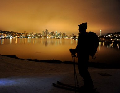 On record snow, night skier with pack and head light, city reflected in Lake Union, Space Needle, from the top of the hill, Gas Works Park, Wallingford, Seattle, Washington, USA photo