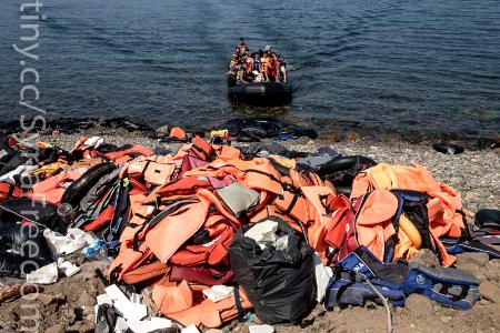Migrants and refugees arrive by dinghy behind a huge pile of life vests after crossing from Turkey photo