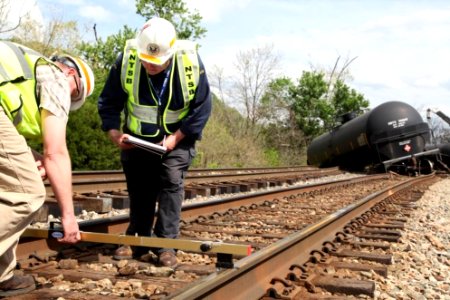 A view looking east at the last car derailed in the background while investigators are taking measurements of the track geometry