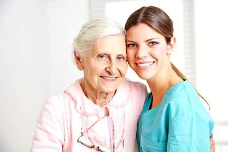 Smiling caregiver embracing happy senior woman in nursing home