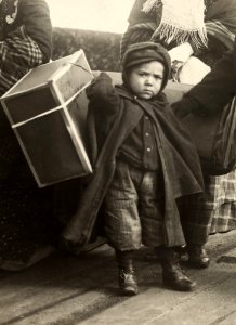 An immigrant boy carries luggage at Ellis Island.