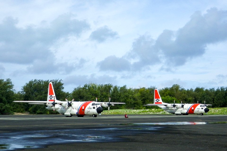 Two U.S. Coast Guard C-130 aircraft parked in front of the NAF Hangar
