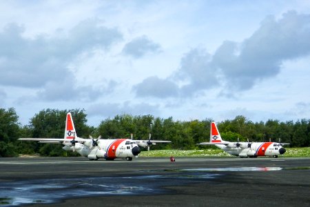 Two U.S. Coast Guard C-130 aircraft parked in front of the NAF Hangar