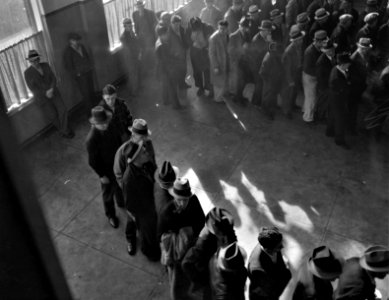 Shuffle With Tired Feet: Line of men inside a division office of the State Employment Service office at San Francisco, California, waiting to register for benefits on one of the first days the office was open. January 1938. photo