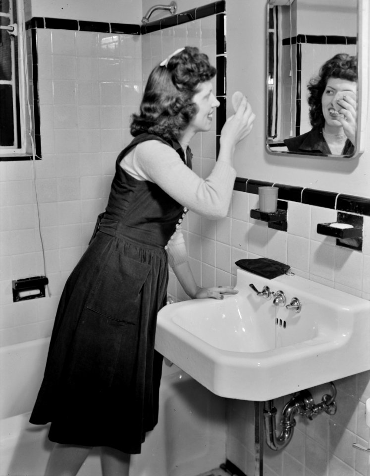 Touching Up: A young stenographer has the use of a bathroom to powder her nose and wash while she works for the Foreign Function Bureau, housed in a converted apartment building. Washington, D.C.. December 1941.