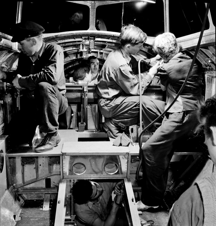 From the Hands of Many: A skilled team of men and women workers at the Boeing plant in Seattle complete assembly and fitting operations on the interior of a fuselage section for a new B-17F (Flying Fortress) bomber, 1942.