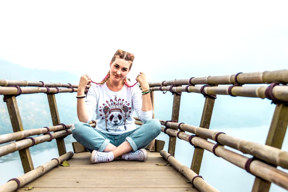 Young woman sitting on the wooden bridge on the top of the mountain with a tropical lake background. Bali island.