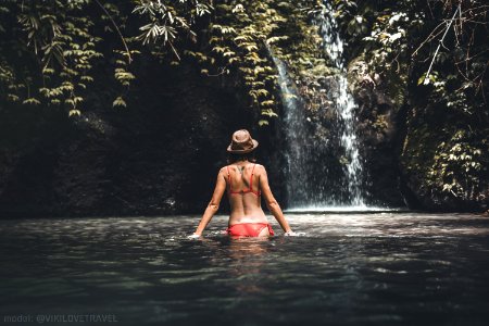 Rear view of Young woman tourist with straw hat in the deep jungle with waterfall. Real adventure concept. Bali island. photo