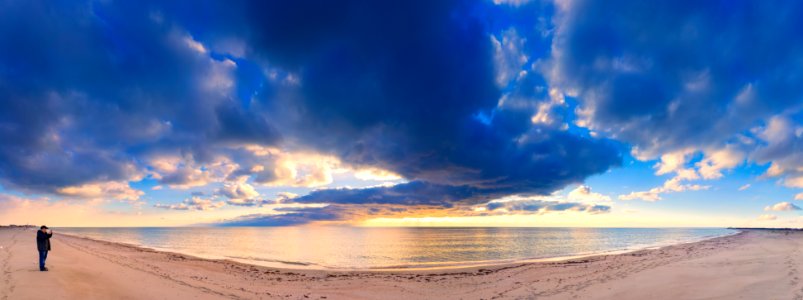 Dramatic natural landscape: cold leaden clouds reflecting in the sea, the skyline and a man standing on the sand (Panoramic landscape) photo