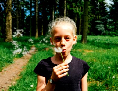 woman in black shirt blowing dandelion