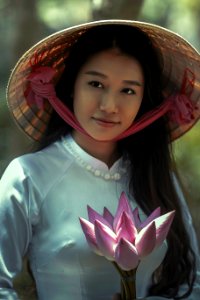 woman wearing white long-sleeved dress and brown sungat holding pink petaled flower photo