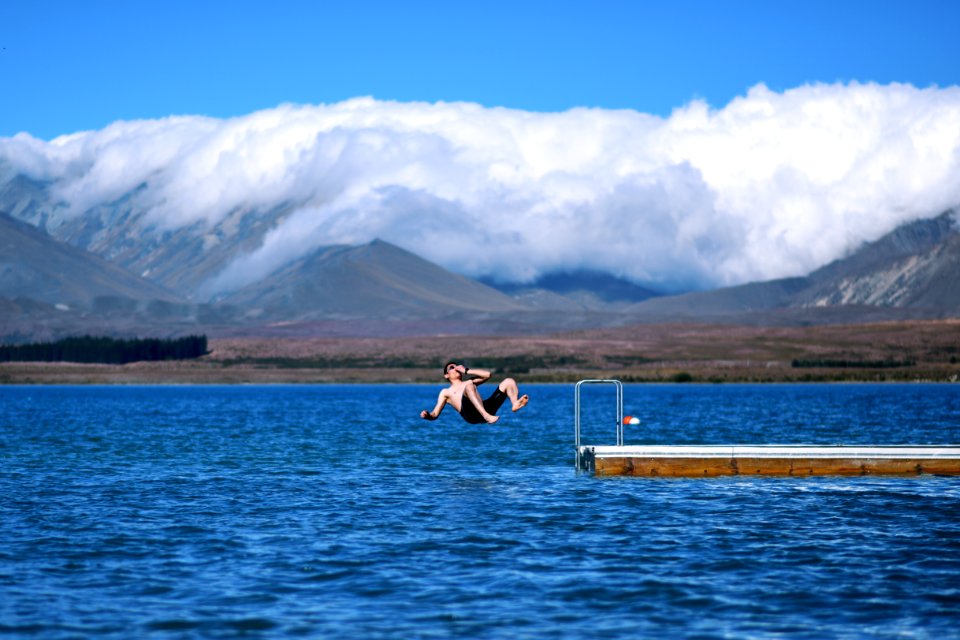 man jumps on body of water holding his nose