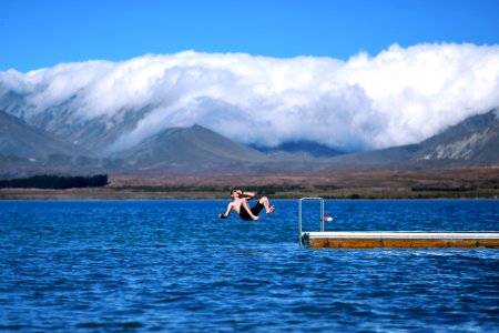 man jumps on body of water holding his nose photo