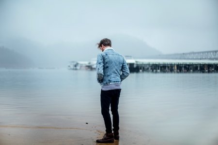 man in blue denim jacket standing on shore photo