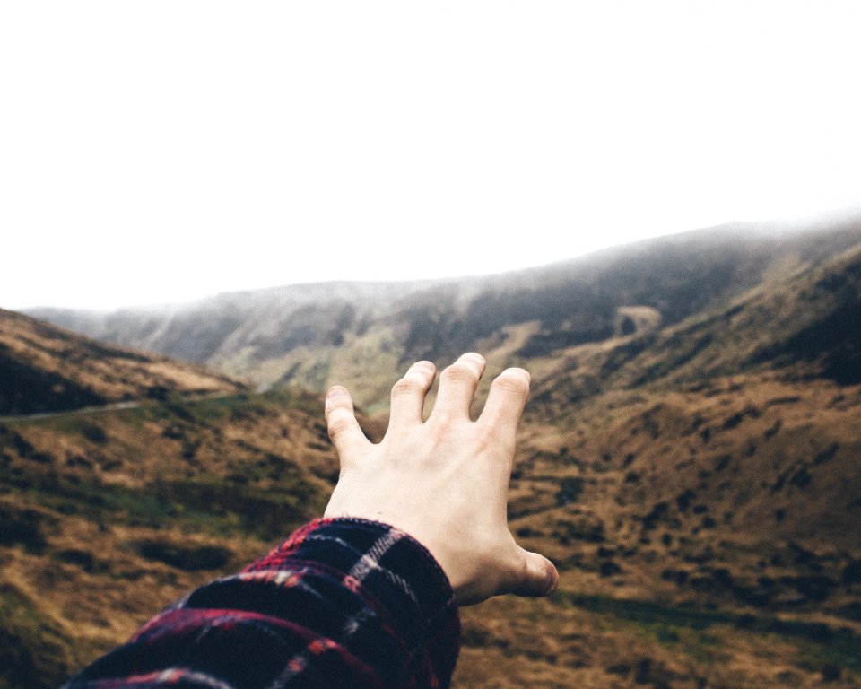 point of view photography of person raising hand towards mountains