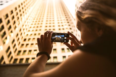 selective focus photography of woman taking low angle photo of high-rise building photo