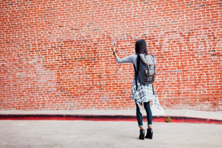 woman standing beside cinder brick wall while using smartphone photo