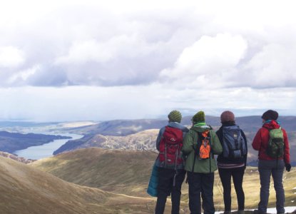 four person standing while looking on mountain view with body of water at daytime photo