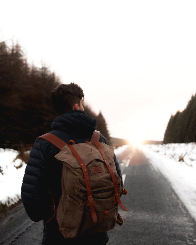 man with backpack standing in middle of road at daytime photo