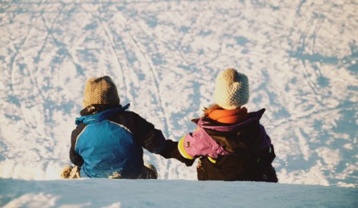 two people sitting on snow during daytime photo