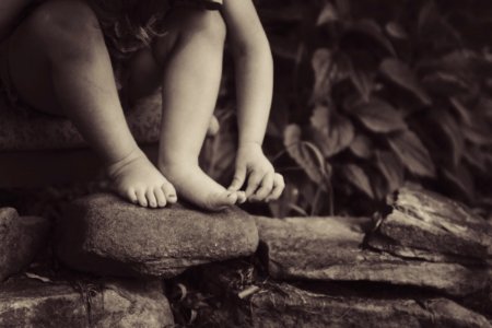 depth photography of child sitting on rock beside plant photo