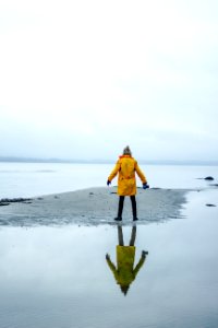person in yellow coat on gray sand surrounded by water