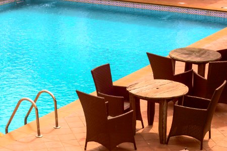 wooden cafe table and chairs beside inground pool photo