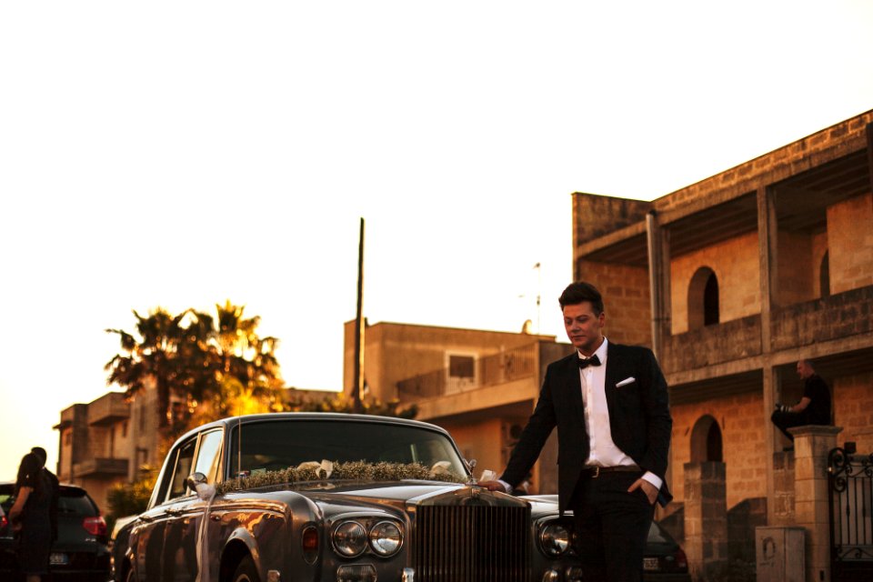 man wearing black suit jacket standing near gray car