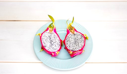 2-sliced dragon fruit in ceramic plate placed on wood plank