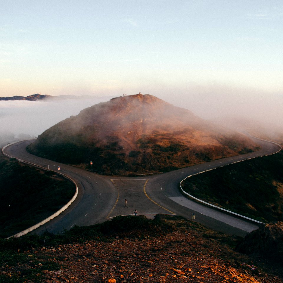 bird's-eye view photo of two people standing on gray concrete road in front of hill
