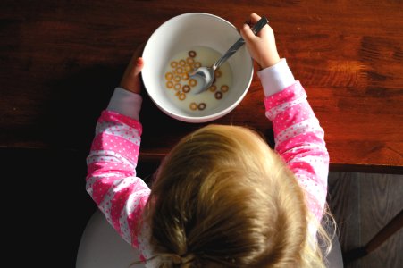 girl eating cereal in white ceramic bowl on table photo