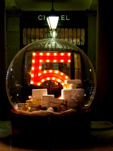 A large glass ball with the number 5, full of Chanel products in front of their storefront. photo