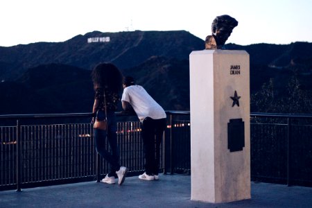 two man and woman leaning on railing and Hollywood Sign at the distance during day photo