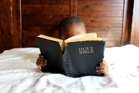 boy reading Holy Bible while lying on bed photo
