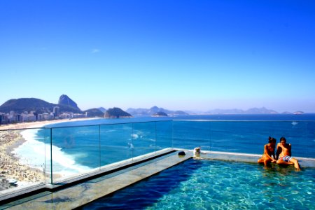 A couple sitting on the edge of a swimming pool overlooking a crowded beach and a deep blue sea photo