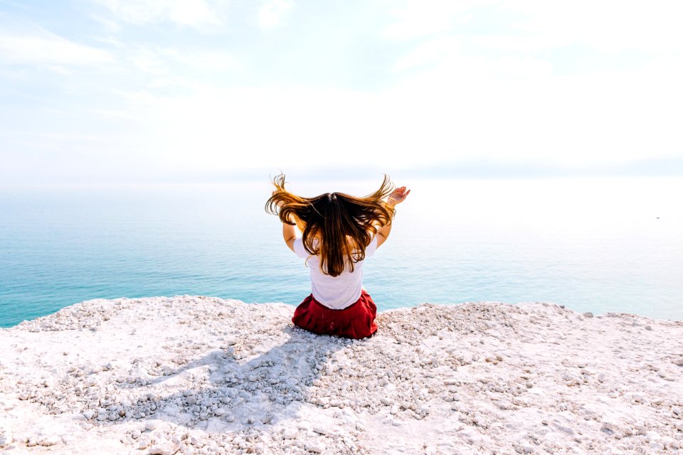 woman sitting on cliff near body of water