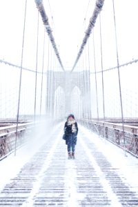 woman wearing black fur-lined coat standing on the bridge with snow during daytime photography photo