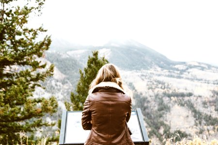 back photo of woman wearing black leather jacket in front of snowed mountain photo