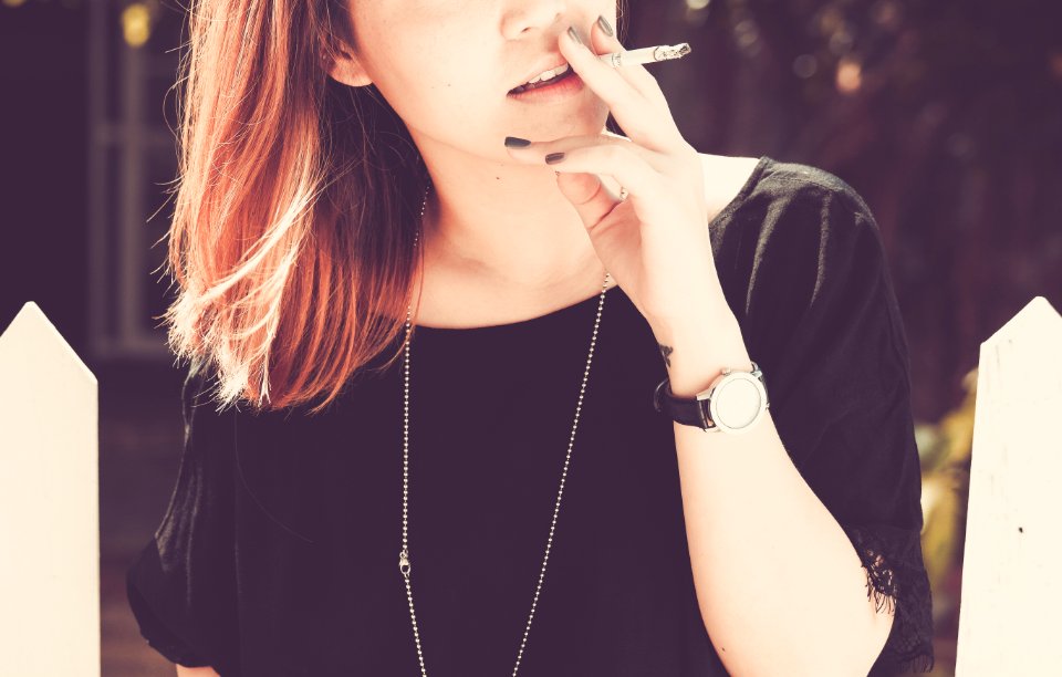 woman smoking beside white fence