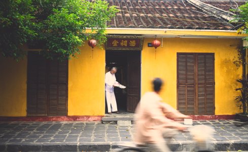 Asian house with a man in the door and another man on a bike driving by photo