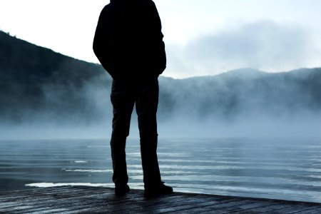 man standing facing body of water under white sky photo