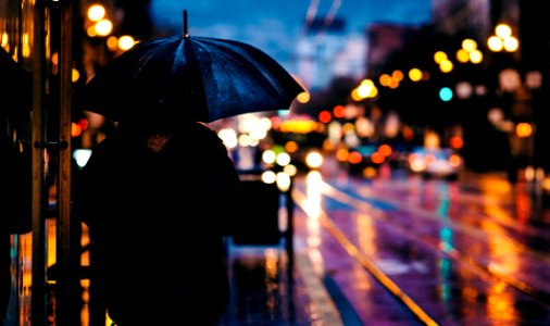 person walking on street while holding black umbrella near cars on road at nighttime photo