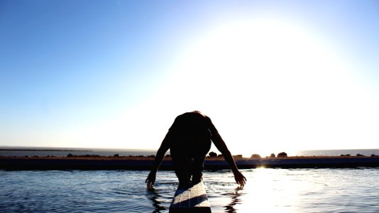 person kneeling on wood surface surrounded by body of water
